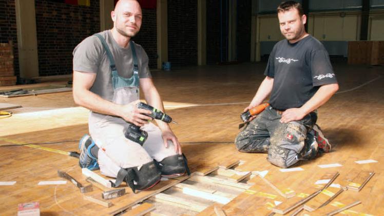 Parkettbodenleger Tobias Badel (l.) und Mathias Trapp von Firma Jürs aus Probst Jesar bei Arbeiten in der Ventschower Sporthalle. 