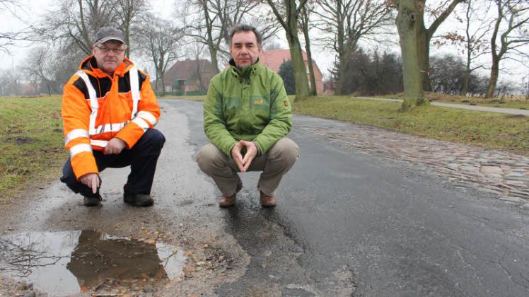 Bürgermeister Rainer Schmidt (l.) zeigt auf eines der Schlaglöcher, die die Ortsdurchfahrt „zieren“. Er sowie Wilfried Saß setzen sich schon seit vielen Jahren dafür ein, dass  der desolate Straßenzustand behoben wird. 