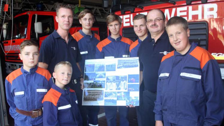 Jugendwart Karl-Heinz Sauerbaum (2. v. r.) und sein Stellvertreter Mario Rieck (2. v. l.) mit einem kleinen Teil des Feuerwehrnachwuchses und Fotos aus der Gründerzeit der Wehr  