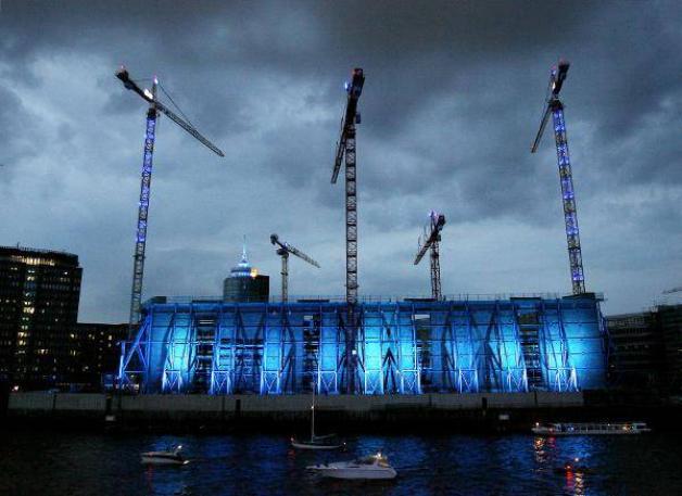 Die Baustelle der Elbphilharmonie ist in Hamburg während der "Cuise-Days" blau angeleuchtet (02.08.2008). Es stand damals bereits im Raum, dass der Termin der Fertigstellung um Jahre nach hinten rücken würde. Foto: dpa