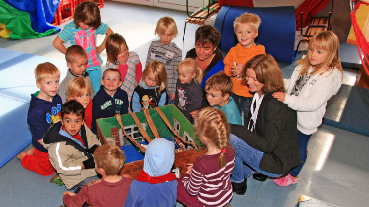 Leiterin Anke Petersen (2. v. r.) und Astrid Lorenzen begutachten zusammen mit den Kindern eines der Pappmodelle für die Kita-Erweiterung. 