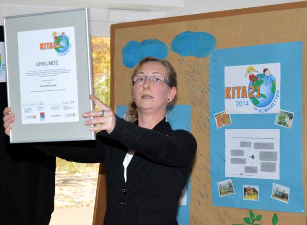 Kita-Mitarbeiterin Gabi Schneider zeigt den Kindern die Auszeichnung. 