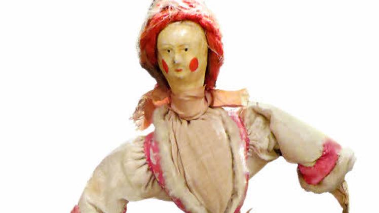 Originalpuppe aus der Wunderkammer von Halle. Die kleine Figur trägt ein Kleid aus Schafsfell mit roten Lederapplikationen, darüber eine Schürze aus Leinen. Die Schuhe sind mit Stickereien geschmückt.  

