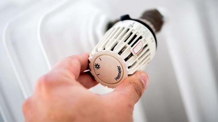 Ein Mann dreht in einer Wohnung am Thermostat einer Heizung
