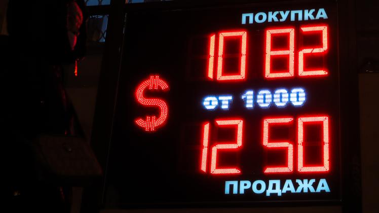 Passanten gehen an einer Wechselstube vorbei, an der auf einer Anzeige der Wechselkurs des Rubels zum US-Dollar zu sehen ist.