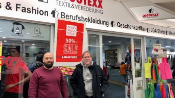 „Logotexx“-Mitarbeiter Wahbeh Nour Eddin und Inhaber Erich Barkhau gemeinsam vor dem Ladeneingang des Textildruck-Geschäfts. 