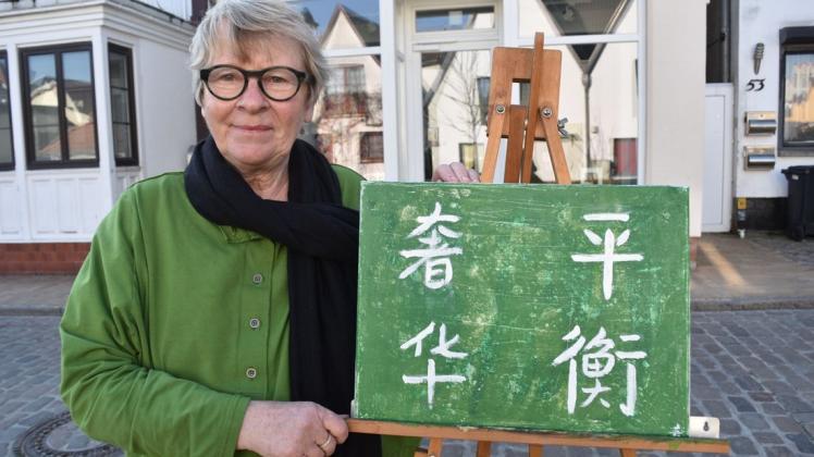 Galeristin Petra Bannier zeigt ein Bild, auf dem in chinesischen Schriftzeichen der Name ihrer Galerie „Balance  & Luxus“ steht. Das Gemälde hat die Warnemünder Therapeutin Ziyun Zhang als Geschenk für sie gemalt.