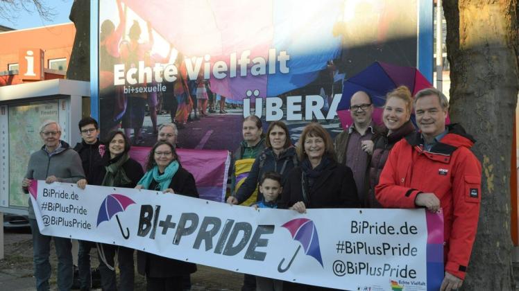 Verantwortliche aus der Politik und Organisator Frank Thies (hinten rechts mit Regenschirm) vor dem neuen Plakat, das in der Friedrich-Ebert-Straße in Pinneberg hängt.