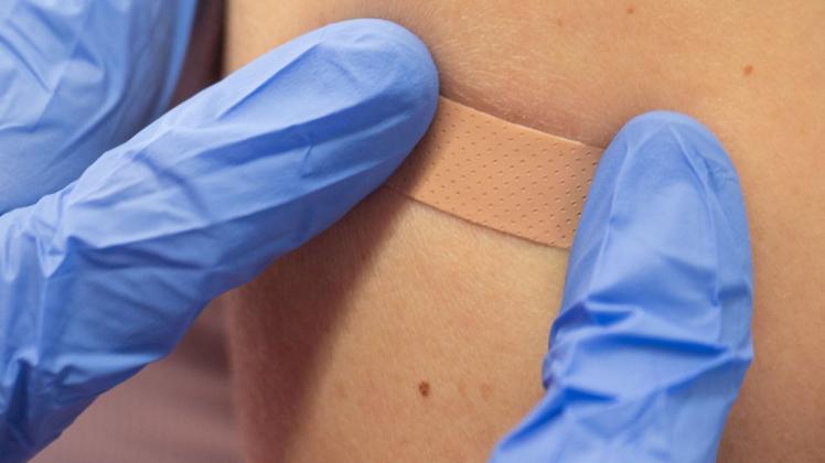 Eine medizinische Fachkraft klebt nach einer Novavax-Impfung ein Pflaster auf einen Oberarm.