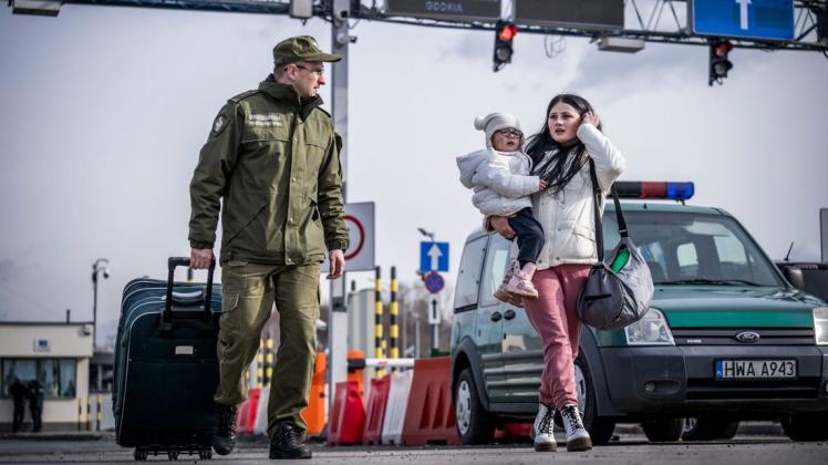 Ein Grenzbeamter hilft einer Geflüchteten aus der Ukraine nach ihrem Grenzübertritt von Schehyni in der Ukraine nach Medyka in Polen mit ihrem Gepäck.