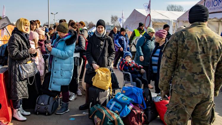 Geflüchtete aus der Ukraine warten kurz hinter der Grenze zur Ukraine am Grenzübergang Medyka darauf, von Helfern in Empfang genommen zu werden.