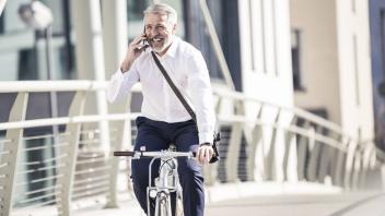 Happy mature businessman talking on cell phone and riding bicycle on a bridge in the city model rele