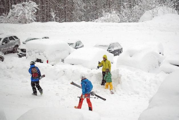Skiurlauber in Österreich suchen auf einem Parkplatz ihr eingeschneites Auto. 