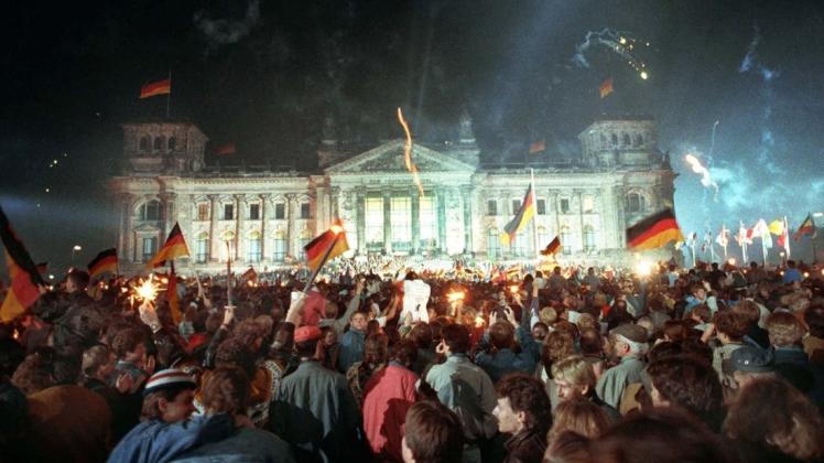 Jubelnde Menschenmassen vor dem Berliner Reichstag, die mit Feuerwerk, Deutschlandfahnen und Volksfesttrubel am 3. Oktober 1990 die wiedergewonnene Einheit Deutschlands feiern. Foto: dpa/Jörg Schmitt