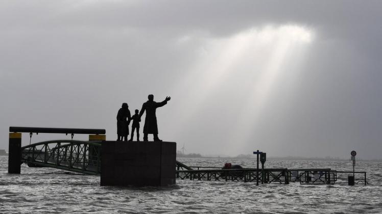 Sonnenstrahlen brechen durch die Wolken am Auswandererdenkmal auf dem überfluteten Willy-Brand-Platz. Foto: dpa/Carmen Jaspersen