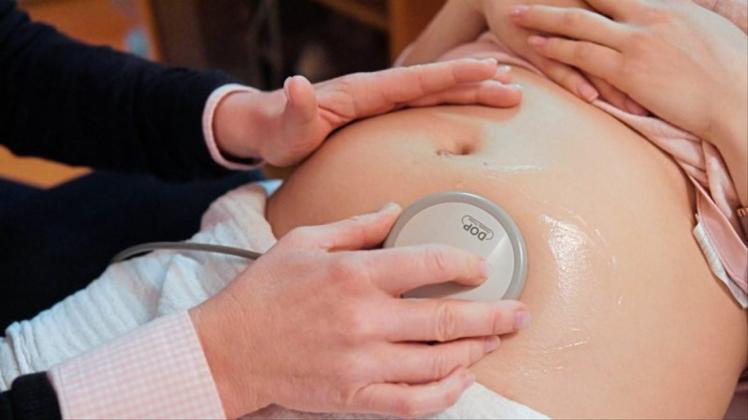 Eine Hebamme hört die Herztöne eines Babys einer Schwangeren ab. 