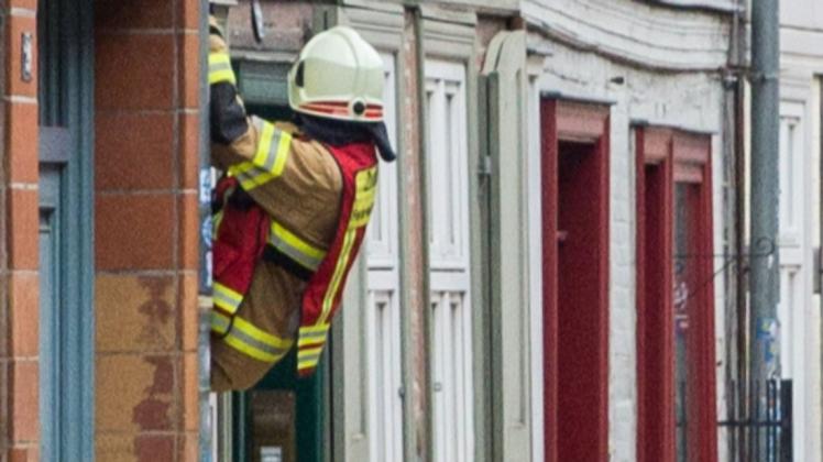 Ein Feuerwehrmann der Schweriner Berufsfeuerwehr klettert durch ein Fenster in eine Wohnung in der Münzstraße.