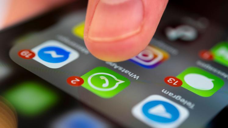 Finger tippt auf Bildschirm mit App Symbolen von Messenger-Diensten und sozialen Netzwerken, WhatsApp, Facebook, Telegra
