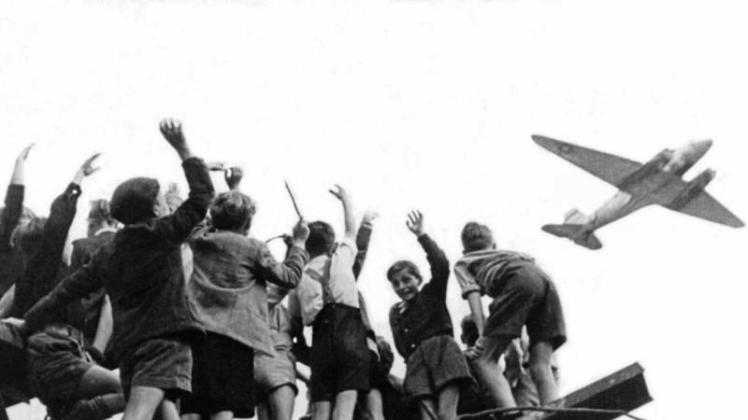 West-Berliner Jungen stehen 1948 auf einem Trümmerberg und winken einem sogenannten Rosinenbomber zu. 