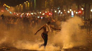 Ein Mann tritt eine von der Polizei geworfene Tränengasgranate während Ausschreitungen auf der Champs Elysees.