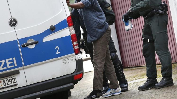 Ein Polizist durchsucht während einer Razzia in einer Gemeinschaftsunterkunft für Asylbewerbe den Schuh eines Asylbewerbers. Foto: dpa