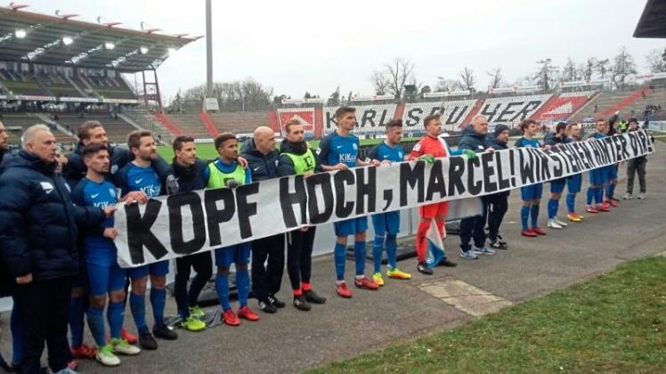 Die Spieler und Trainer des SV Meppen halten nach dem Spiel gegen den KSC ein Banner hoch, das einem Fan gewidmet ist. 