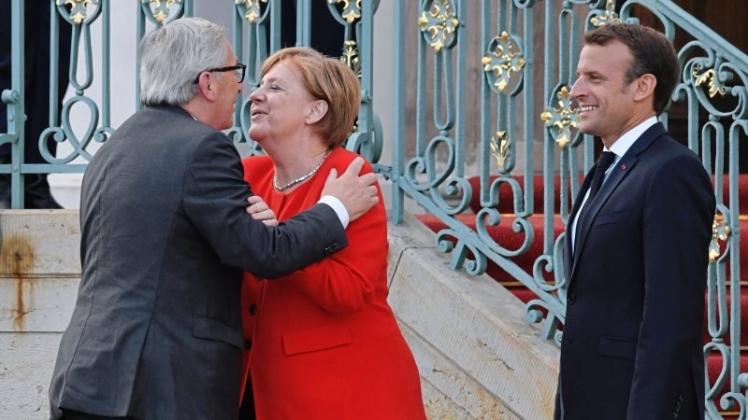 Küsschen von der Kanzlerin: EU-Kommissionschef Jean-Claude Juncker (links) und Frankreichs Präsident Emmanuel Macron werden von Angela Merkel im Barockschloss Meseberg empfangen. 