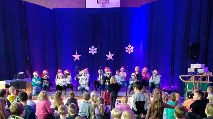 „Let it shine“ (Lass es leuchten) ruft die Klasse 3a in ihrem musikalischen Beitrag mit Weihnachtsmannmützen und Sonnenbrillen dem Publikum zu. 