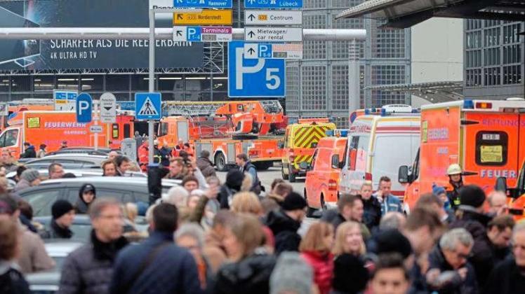 Reisegäste warten am Hamburger Flughafen zwischen Fahrzeugen der Feuerwehr auf Anweisungen. 