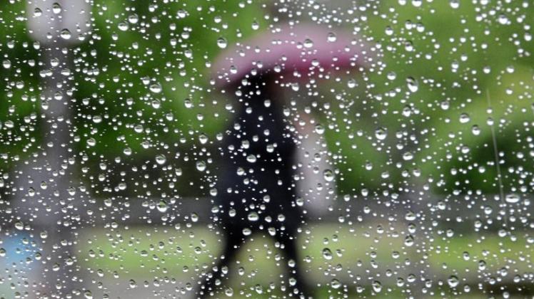 Eine Frau mit Regenschirm geht am 28.05.2014 in Eschwege (Hessen) an einem mit Regentropfen überzogenen Autofenster vorbei. Im Nordosten Hessens soll es den ganzen Tag regnen. 