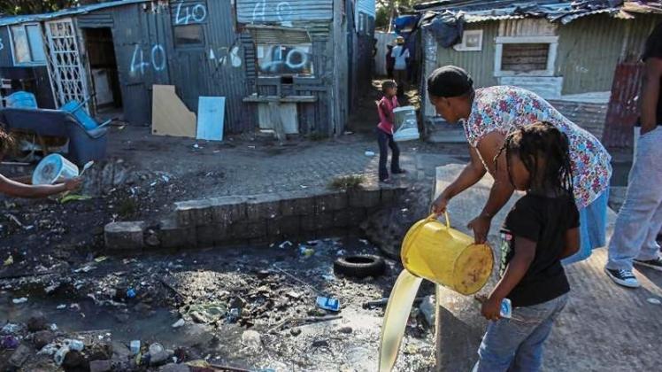 Bewohner von Kapstadt schütten nahe einer Entnahmestelle für sauberes Wasser ihr Abwasser in einen Fluss. 