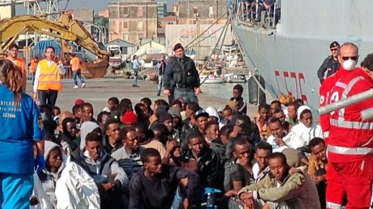 Angekommen: Eine Gruppe von Flüchtlingen sitzt inn einem italienischen Hafen, nachdem die Menschen ein italienisches Marineschiff verlassen haben, das sie gerettet hat. 