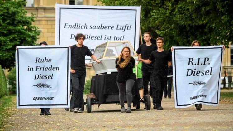 Greenpeace-Aktivisten ziehen einen Sarg mit einem 1,6 Liter Diesel-Motor des Volkswagenkonzerns. Dazu tragen sie Banner mit den Aufschriften „Ruhe in Frieden Diesel“, „Endlich saubere Luft! Der Diesel ist tot!“ und „R.I.P. Diesel“. 