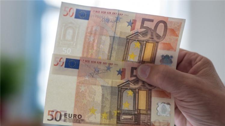 Ein echter (oben) und ein gefälschter 50-Euro-Schein sind im Licht eines Geldprüfers zu sehen. 