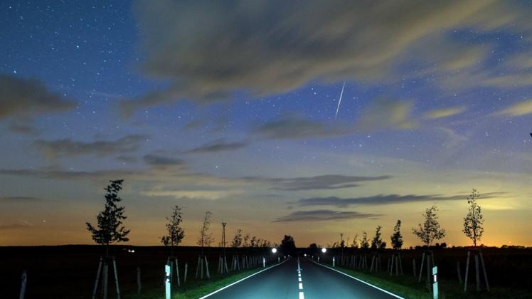 Eine Sternschnuppe leuchtet am Nachthimmel über einer Landstraße. Sternschnuppen sind für Fotografen eine groe Herausforderung. 