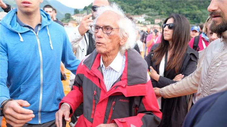Künstler Christo wird vor Paratico auf dem Lago d’Iseo in Italien von Begleitern durch die Besuchermassen über die schwimmenden Stege mit orangefarbenen Stoff seines Projekts „The Floating Piers“ geführt. Künstler Christo wird vor Paratico auf dem Lago d’Iseo in Italien von Begleitern durch die Besuchermassen über die schwimmenden Stege mit orangefarbenen Stoff seines Projekts „The Floating Piers“ geführt.