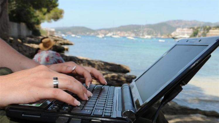 Eine Frau arbeitet am Strand von Santa Poca auf Mallorca mit ihrem Laptop am Wasser. 