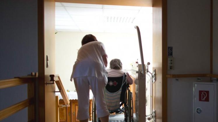 Eine Pflegerin hilft einer Bewohnerin einer Altenpflegeheimes mit einer Rollstuhlhilfe eine Treppe hinauf. 