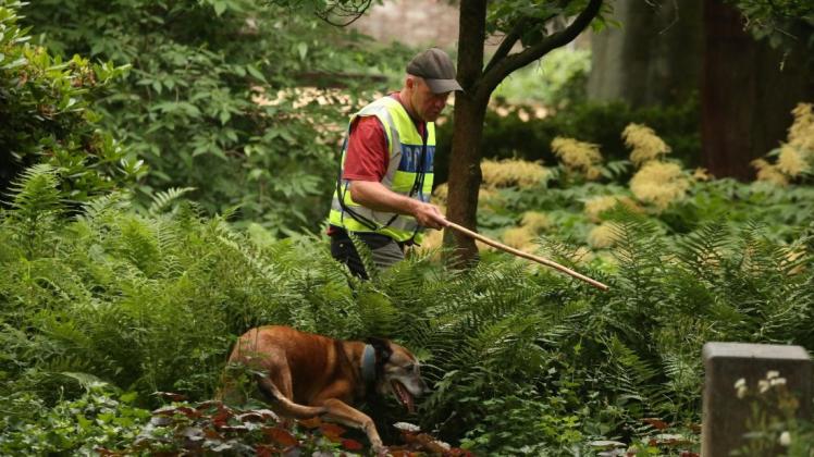 Ein Polizist durchsucht zusammen mit einem Spürhund ein Gebüsch im Viersener Casino Garten. Dort war am Montag ein Mädchen niedergestochen worden. 