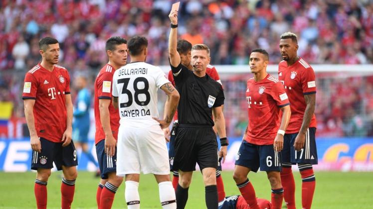 Unter den Blicken der Bayern-Spieler zeigt Schiedsrichter Tobias Welz (M) die Rote Karte gegen Karim Bellarabi (38) von Leverkusen, während der gefoulte Bayern-Spieler Rafinha verletzt am Boden liegt. Foto: Tobias Hase/dpa
