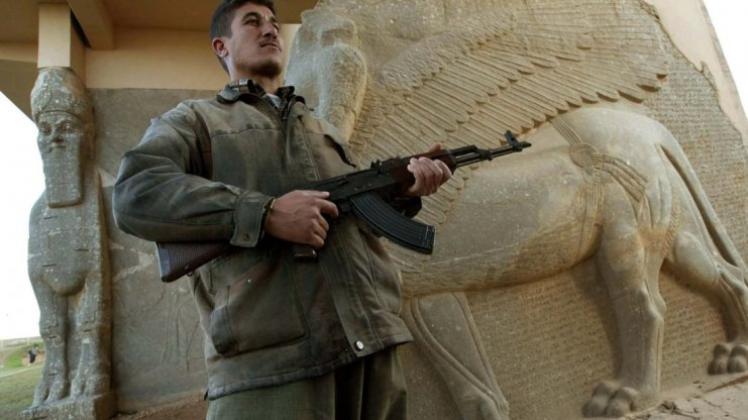 Schutz für Kulturgut? Der ist in Ländern wie dem Irak nicht mehr garantiert. Hier steht ein Wächter 2003 mit seiner Waffe vor einer Wandskulptur in der archäologischen Stätte der ehemaligen assyrischen Haupstadt Nimrud (auch Kalach oder Kalchu genannt). Inzwischen haben Kämpfer der Terrormiliz Islamischer Staat den Ort gesprengt. 