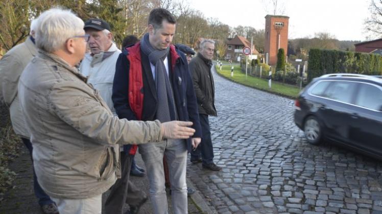 „Beeindruckt“ vom Zustand der Dorfstraße: Der Fraktionsvorsitzende der FDP im Landtag, Christian Dürr, lässt sich von den Anwohnern die vielen Risse im Kopfsteinpflaster der Straße zeigen. 