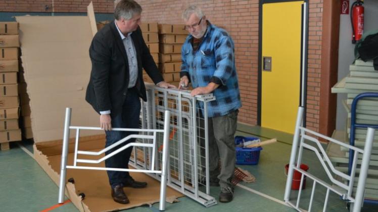 Bürgermeister Herwig Wöbse und Peter Sparkuhl packen ein Bettgestell aus, das in der Delme-Turnhalle aufgebaut wird. 