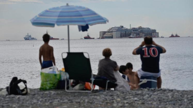 Italien: Strandbesucher beobachten das Wrack der „Costa Concordia“, das in den Hafen von Genua geschleppt wird. 