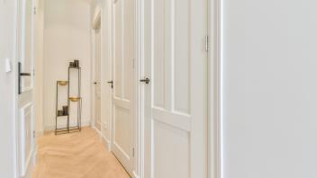 Long empty hallway with various closed white room doors and creative decorations on stand placed in light apartment at h