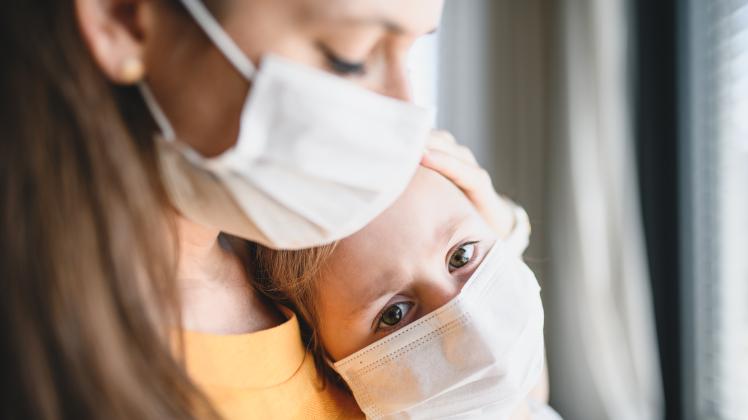 Mother and child with face masks indoors at home, Corona virus and quarantine concept.