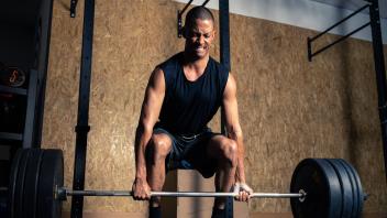 Full body of strong African American male powerlifter in activewear lifting heavy barbell during weightlifting workout i