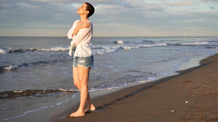 Young woman hugging herself while standing at beach model released Symbolfoto VEGF04746