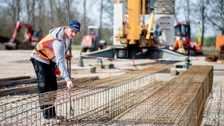 Ein Auszubildender in einem Bauunternehmen hakt  Eisenkörbe für das Fundament an einem Kranhaken ein. Foto: Hauke-Christian Dittrich/dpa/Archivbild