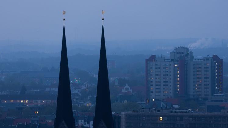 Die Türme der Neustädter Marien-Kirche sind im Dunst in der Morgendämmerung zu sehen. Foto: Friso Gentsch/dpa